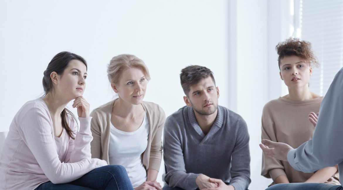 Obraz przedstawia terapeutę przemawiającego do grupy ludzi